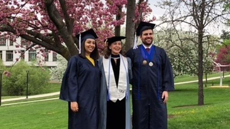 Professor posing with two students under tree in caps and gowns